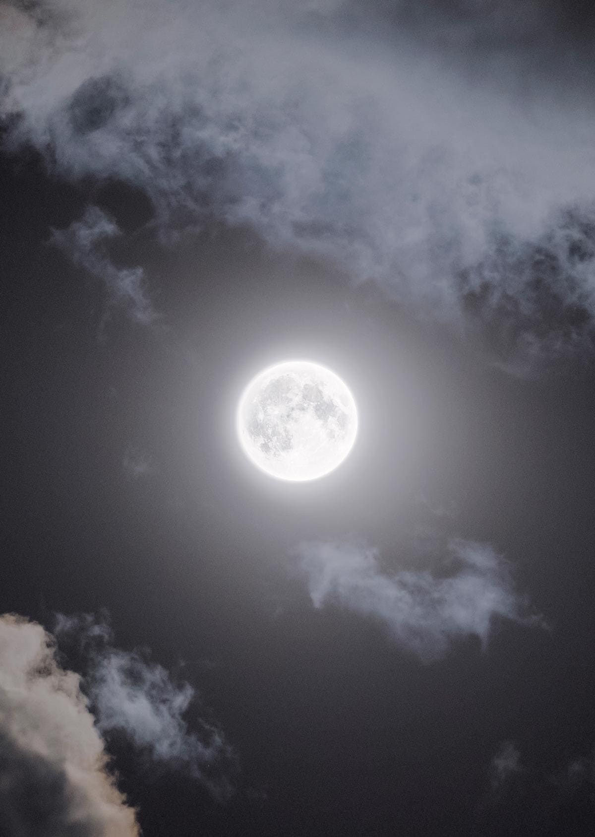 A glowing full moon in the night sky with clouds
